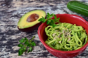 Fresh organic raw zucchini noodles or zoodles with avocado pesto sauce garnish with parsley and sunflower seeds. 
