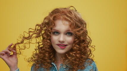 Stylish girl flirting with camera. Cheerful girl playing with curly hair in studio