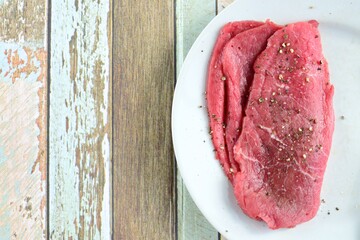 Raw minute steak on a plate. Seasoned with sea salt and black pepper 