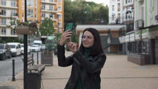 Young happy girl photographs a beautiful city on a smartphone.