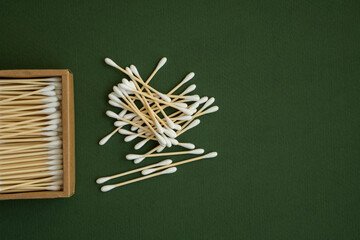 Eco-friendly cotton swabs. A cardboard box containing recyclable bamboo cotton buds on a green surface. Zero waste concept. Eco product. Cosmetic sticks in a box. Wooden sticks for cleaning ears.