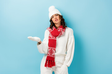 displeased young woman in white winter outfit pointing with hand on blue