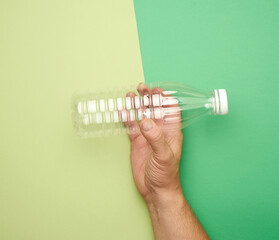 male hand holding empty transparent plastic bottle on green background