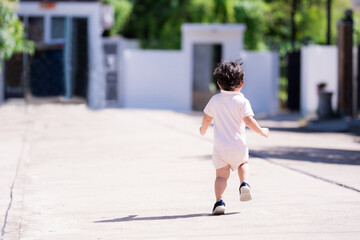 Back side of little boy was jogging on a concrete road. Summer morning or spring. Happy child is 3 years old.