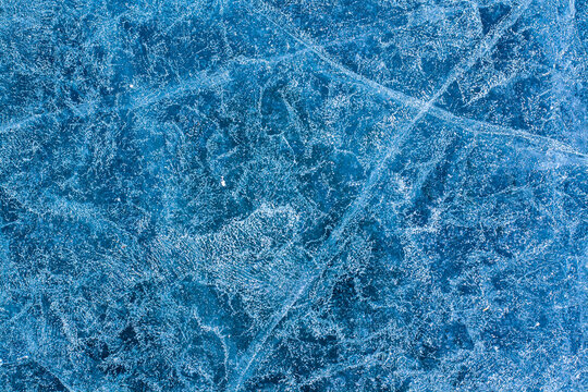 Unique background texture of ice. Winter pattern on the blue ice of the lake. Cracks and air bubbles. Horizontal.