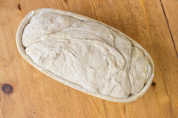 Sourdough bread rising in basket on wooden surface