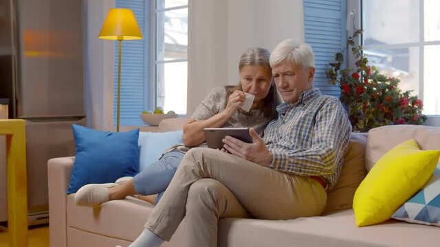 Upset elderly couple receiving bad news on digital tablet at home