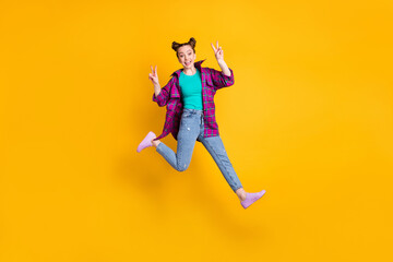 Full size photo of attractive lady jump show v-sign symbols greet friends meeting after self isolation wear casual plaid magenta shirt jeans sneakers isolated yellow vivid color background