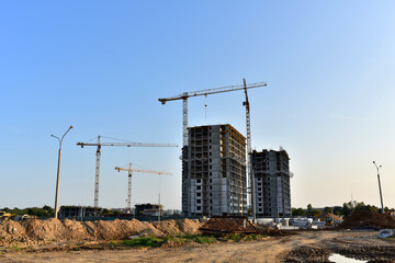 Tower cranes working at construction site on blue sky background. Construction process of the new modern residential buildings