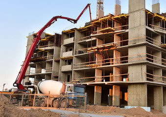 Builder workers during formworks and pouring concrete through a сoncrete pump truck connected to a ready-mixed truck. Concrete line and boom pumping at construction site. Tower cranes working