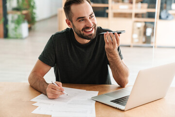 Happy man smiling and talking on cellphone while working with laptop