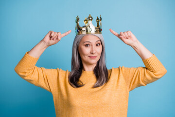 Closeup headshot photo of charming gorgeous pretty senior lady golden crown head pointing fingers egocentric loving herself concept wear yellow jumper bright blue color background © deagreez