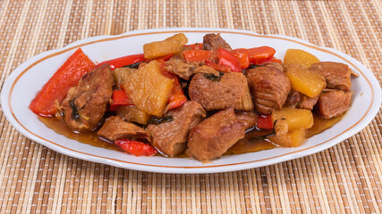 Adobe pork with pineapple and bell pepper in an oval plate on a bamboo napkin - philippine cuisine