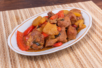 Adobe pork with pineapple and bell pepper in an oval plate on a bamboo napkin - philippine cuisine