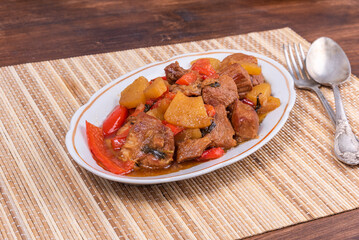 Adobe pork with pineapple and bell pepper in an oval plate on a bamboo napkin - philippine cuisine