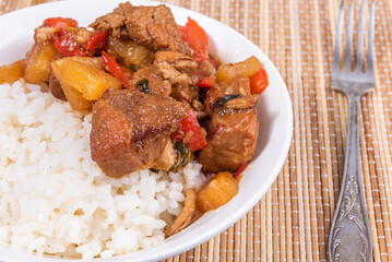 Adobo pork with pineapple and pepper in a bowl of boiled rice on a bamboo napkin, closeup - Philippine cuisine