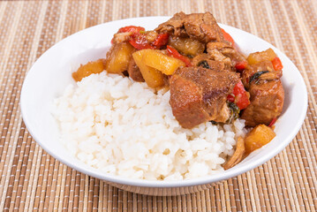 Adobo pork with pineapple and pepper in a bowl of boiled rice on a bamboo napkin, closeup - Philippine cuisine