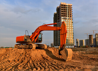 Excavator during excavation at construction site on sunset background. Red Backhoe on road work....