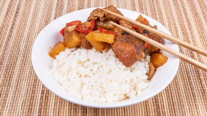 Adobo pork with pineapple and pepper in a bowl of boiled rice and chopsticks on a bamboo napkin, close up - Philippine cuisine