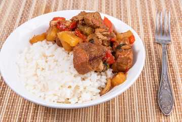 Adobo pork with pineapple and pepper in a bowl of boiled rice on a bamboo napkin, closeup - Philippine cuisine