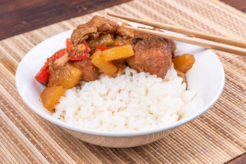 Adobo pork with pineapple and pepper in a bowl of boiled rice and chopsticks on a bamboo napkin, close up - Philippine cuisine