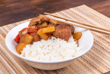 Adobo pork with pineapple and pepper in a bowl of boiled rice and chopsticks on a bamboo napkin, close up - Philippine cuisine