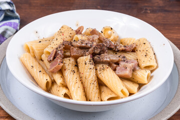  Pasta alla gricha with pancetta in a plate on a dark wooden table close up