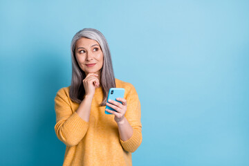 Photo of minded old woman use smartphone look copyspace touch fingers chin think thoughts decide...