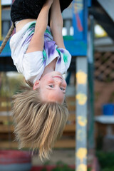 Beautiful little girl hangs upside down on the playground. Little girl smiles into the camera.