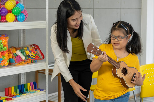 Autistic, Autism Or Down Syndrome Children Girl Is Playing The Ukulele With Her Teacher. Concept Disabled Child Learning In School.