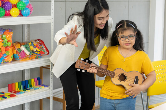 Autistic, Autism or Down Syndrome children girl is playing the ukulele with her teacher. Concept disabled child learning in school.