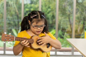 Autistic, Autism or Down Syndrome children girl is playing the ukulele. Concept disabled child learning in school.