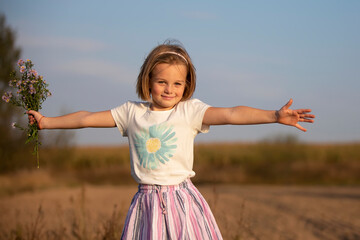 Happy little girl in the meadow with a bouquet of flowers. A child on a beautiful summer field with developing hair.