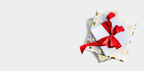 Fototapeta premium A group of white and gold gift boxes tied with a red ribbon bow on a light table. Top view, flat lay. Composition for birthday, Valentine's Day or Christmas, banner background, copy space.