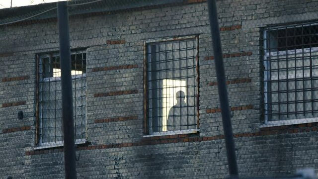 A silhouette of a prisoner in a prison window. The man looks out of the window.