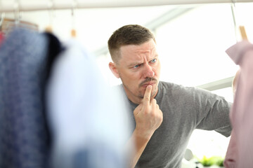 Pensive man looks at hanger with clothes. Men's wardrobe and stylish clothing concept