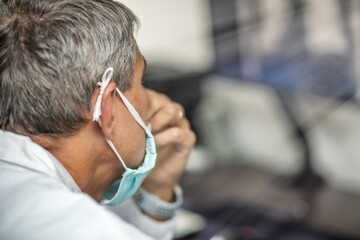 Male doctor wearing mask in covid-19 department looking at patient x-ray on the computer screen