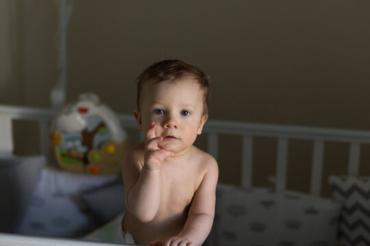 Cute caucasian baby boy wearing only diaper standing in a crib. Image with selective focus