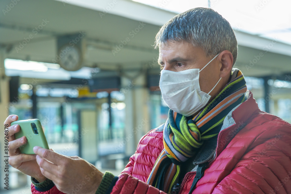 Poster man with health mask using smartphone at empty railway station in covid pandemic