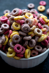 Colorful cornflakes rings in bowl isolated on dark background. Morning breakfast for kids.