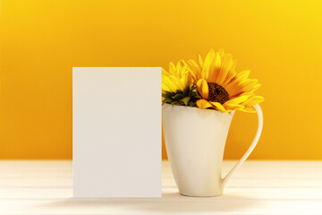 Greeting card mockup with white cup and sunflowers. Empty postcard with space for text. Template with porcelain cup and yellow flowers. Bright yellow background.