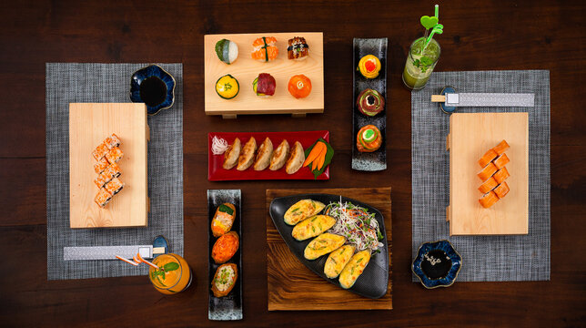 Elevated view of the table with Japanese cuisine various side dishes and coctails. Philadelphia, Tuna uramaki, Flower sush set, Gyoza, Baked mussles, tuna uramaki, onigiri sushi and inari sushi set