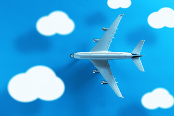 Top view of a commercial plane with clouds and long shadow on a blue background.