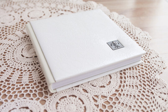 White photo book with leather cover. Stylish wedding photo album.  Family photoalbum on the table . Beautiful notepad or photobook with elegant openwork embossing on a wooden background.