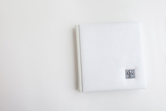 White photo book with leather cover. Stylish wedding photo album.  Family photoalbum on the white table . Beautiful notepad or photobook with elegant openwork embossing on a white background.