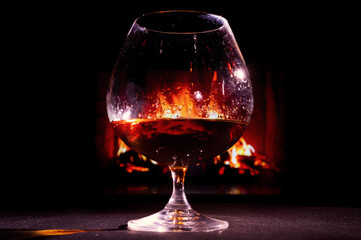 Close-up on a glass of brandy in the dark on the background of the fireplace