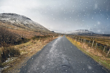 Empty small road in a mountains on a winter day with snow falling. Peaks covered with snow. Clear sky. Gleniff Horseshoe Drive, county Sligo, Ireland. Popular tourist route and destination