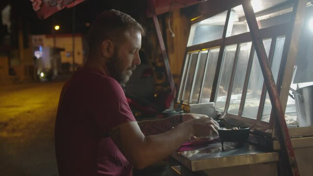 A young caucasian bearded man eating a torta in a street food stand at night in Valladolid, Mexico