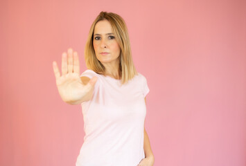 Young beautiful woman wearing casual t-shirt over pink background doing stop sing with palm of the hand. Warning expression with negative and serious gesture on the face.