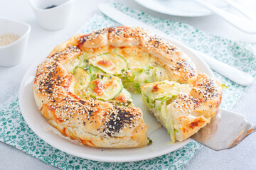 Open puff pastry zucchini pie sprinkled with poppy seeds and sesame seeds with a cut piece, selective focus